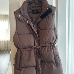 Brun väst - En mellanlång väst från Bikbok med snörning och dragkedja. Säljs då den inte kommer till användning längre. Xs men oversized.