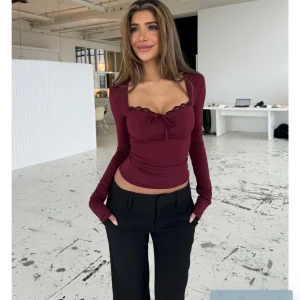 Vinröd långärmad topp med spetskant - Säljer en vinröd långärmad topp med croppad passform. Toppen har en söt rosettdetalj framtill, spetskant vid urringningen och figurnära siluett. Perfekt för dig som gillar trendiga och feminina plagg med snygga detaljer.