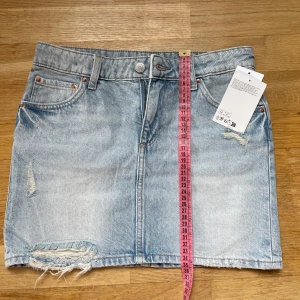 Ljusblå jeanskjol med slitningar - Snygg ljusblå jeanskjol i kort modell med slitna detaljer och rå kant nertill. 