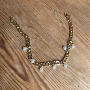 Chunky guldhalsband med pärldroppar - Stilrent halsband med tjock guldfärgad kedja och hängande droppformade pärlor. Statement piece som ger en lyxig känsla och passar perfekt till en enkel tröja eller skjorta. Kedjan har en klassisk karbinhake och pärlorna är vita med fin glans. Köpt hos LAB Sthlm smycken.