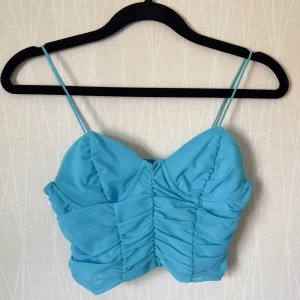 Turkos croppad linnetopp Gina Tricot - Supersöt turkos croppad linnetopp från Gina Tricot med tunna axelband och snygg rynkad front. Toppen har hjärtformad byst och är perfekt för varma dagar. Materialet är lätt och känns skönt mot huden. Passar dig som gillar färg och vill sticka ut lite extra.