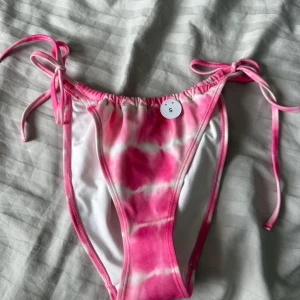 Rosa och vit bikiniunderdel från monki - Snygg bikiniunderdel från monki i rosa och vitt med batikmönster. Modellen har höga ben och knyt i sidorna för perfekt passform. Tillverkad i återvunnen polyester och elastan, perfekt för strandhäng eller poolparty.