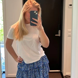 Blå volangkjol med leopardmönster - Supersöt blå kortkjol med volanger och leopardmönster i vitt, svart och grönt. Kjolen har resår i midjan och är luftig med flera lager. Perfekt för dig som gillar färg och mönster! Sitter bra på mig som alltid bär storlek S