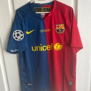FC Barcelona Messi 10 Finaltröja Nike - Säljer en ikonisk FC Barcelona fotbollströja från Champions League-finalen 2009 med Messi 10 på ryggen. Tröjan är halva röd och halva blå, har gula detaljer, klubbmärke och Unicef-logga framtill samt Champions League-märke på ärmarna. Tillverkad i lätt och ventilerande material.