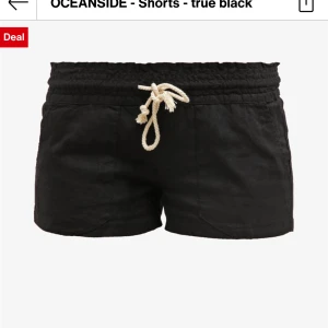 Svarta shorts med snörning från Roxy - Svarta shorts från Roxy i mjukt linnematerial med elastisk midja och vit snörning framtill. Shortsen har två fickor fram och två bak, samt en liten broderad logga på ena bakfickan. Perfekta för varma sommardagar.