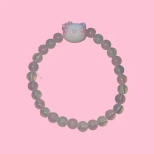 Hello Kitty pärlarmband rosa/vitt - Supergulligt armband med genomskinliga pärlor och en söt Hello Kitty-figur i vitt med rosa detaljer. Perfekt accessoar för dig som älskar kawaii-stil. Vit och ljusrosa om ljuset på bilden säger annorlunda.
