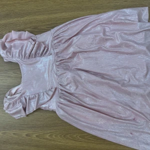 Glittrig rosa klänning - Supersöt glittrig rosa klänning från Zara med volangdetaljer vid axlarna. Klänningen har en lätt skimrande yta och är ärmlös, perfekt för dig som vill sticka ut lite extra. Materialet känns mjukt och följsamt. (barnklänningar) den ena är storlek 110, den andra 104.