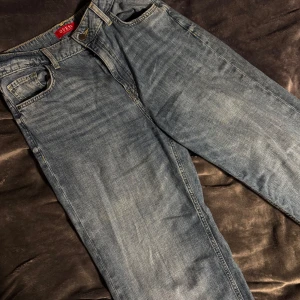 Blåa wide jeans från Guess - Säljer ett par blåa jeans från Guess med klassisk design och snyggt sliten tvätt. Jeansen har hög midja och breda ben för en chill och trendig look. Materialet är jeans med tydliga sömmar och ikonisk Guess-logga på bakfickan. Byxorna är gjorda av ett lätt tyg och passar perfekt för varmt väder.