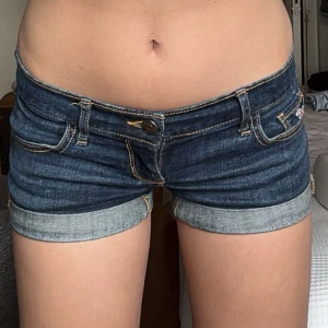 Lågmidjade jeansshorts från Hollister - Snygga lågmidjade jeansshorts från Hollister i klassisk blå denim. Shortsen har uppvikta benslut, dekorativa sömmar på bakfickorna. Dem är som nya men är andvända ett fåtal gånger! Kontakta mig för en minsta fråga🥰( KAN POSTA DEM 15 JULI TIDIGAST!!)