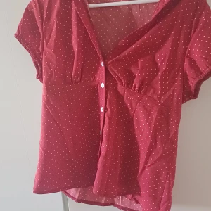 Röd prickig skjorta med knappar - Säljer en röd skjorta med vita prickar och korta ärmar. Skjortan har klassisk krage, vita knappar framtill och lätt figursydd passform. Perfekt för dig som gillar retrovibbar och vill ha något som sticker ut lite extra. Säljer för den va för stor för mig vid bröstet och färgen passa inte mig ❤️ aldrig använt 