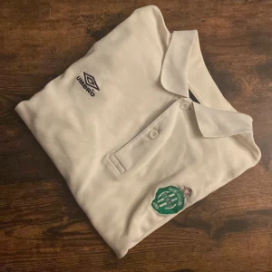 Vintage St. Etienne Pikétröja  - Vintage Umbro piké i storlek L med AS Saint-Étienne-logga. Vit med mörkblå sidor, klassisk retrolook. Perfekt för dig som gillar fotbollscasual och 90-talsstil. Bra skick, inga hål. Sällsynt plagg som sticker ut både på match och i vardagen.