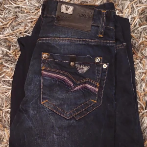 Mörkblå vintage jeans från Armani - Snygga mörkblå jeans från Armani med coola detaljer på bakfickorna och kontrastsömmar. Klassisk femficksmodell med broderad logga och robust känsla. Perfekta för dig som gillar stilrena men ändå unika jeans.                                                               Midjan är storlek 29 men sitter som 30