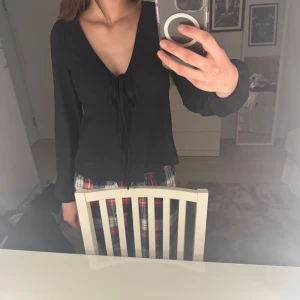 Svart v-ringad topp med knyt - Säljer en svart långärmad topp med djup v-ringning och knyt framtill. Toppen har en figurnära passform och är perfekt att styla till olika outfits. Materialet känns mjukt och stretchigt.