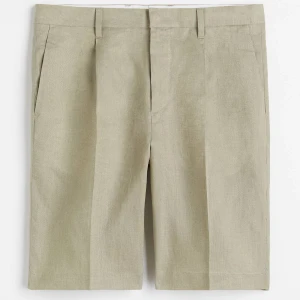 Beige linneshorts med knappdetalj storlek M/L - Snygga beige shorts i linne med klassisk passform och bälteshällor. De har diskreta sidofickor och en bakficka med knapp. Perfekta för varma dagar när du vill vara både bekväm och stilren.