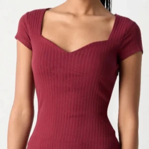Vinröd ribbad klänning med v-ringning plus svart only top - Säljer en vinröd ribbad klänning med korta ärmar och snygg v-ringning. Klänningen har en tight passform och är perfekt för dig som gillar en enkel men stilren look.