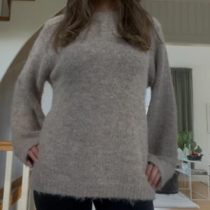 Beige stickad tröja med lång ärm - Mysig beige stickad tröja med lång ärm och rund hals. Tröjan har en lös passform och är perfekt för kyligare dagar. Enkel och stilren design som passar till det mesta.