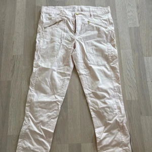 Ljusrosa byxor från Carla F - Säljer ett par ljusrosa byxor från Carla F i mjuk bomullsblandning med dragkedjor vid bensluten och fickor fram och bak. Byxorna har normal passform och är perfekta för vår och sommar. Endast testade 