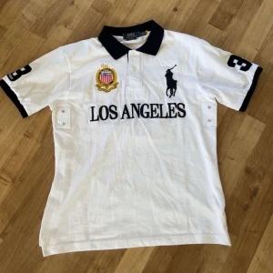 Vit piké t-shirt från Polo Ralph Lauren - Säljer en fet polo Ralph lauren piké som har Los Angeles. Tröjan är perfekt inför sommaren 🏝️🌊☀️🏖️ och även nu på våren tröjan är även i storlek L och är nästan Helt ny och har därför inga skador. Skriv vid frågor ☺️ va lång och tjock