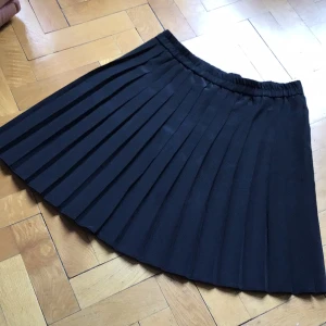 Svart plisserad kjol från Gina Tricot - Snygg svart plisserad kjol från Gina Tricot med resår i midjan. Kjolen har klassiska veck och är perfekt för en trendig och stilren look. Lätt att matcha med olika toppar och skor. Nästan strl XL.