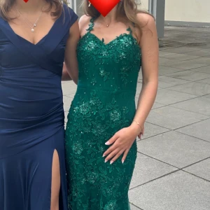 Grön blommig klänning med spetsdetaljer - Säljer nu min fina balklänning! Den är upplagd hos en skräddare som tagit bort mesta delen av släpet. Skärpet över midjan går att ta bort! Den är endast använd en gång och super fin utan några defekter!