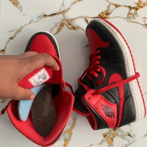 Nike Air Jordans svart och röd - Säljer ett par klassiska Nike Air Jordans i svart och rött med högt skaft. Skorna har röd swoosh, snörning och vit sula. Perfekta för dig som gillar streetstyle och vill sticka ut med en ikonisk sneaker.
