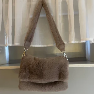 Beige fluffig axelväska från Gina Tricot - Supermjuk och fluffig beige axelväska från Gina Tricot med bred axelrem och silverfärgad logga.