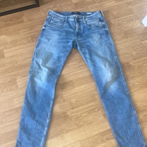 Blå Replay jeansbyxor herr - Säljer ett par klassiska blå jeans från Replay med fem fickor och normal passform. Byxorna har dragkedja, bälteshällor och snygga slitningar för en avslappnad look. Perfekta till vardags och passar till det mesta.