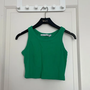 Grön croppad linnetopp - Snygg grön croppad linnetopp med breda axelband och rund halsringning. Perfekt för varma dagar och enkel att matcha med jeans eller kjol.