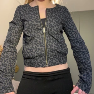 Leopardmönstrad jacka med dragkedja - Säljer en gråsvart leopardmönstrad jacka med dragkedja framtill. Jackan har rund halsringning, långa ärmar och en croppad passform.