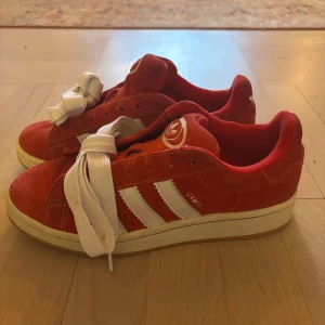 Röda Adidas campus sneakers - Säljer mina superfina adidas campus skor. De är knappt använda så de är i superfint skick. Både box och röda, samt ett par till vita skosnören tillkommer!