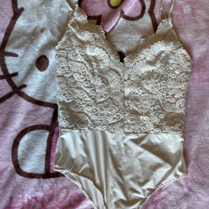 Vit spetsbody från Boohoo - Säljer en vit body från Boohoo med vacker spets upptill och slät satinliknande nederdel. Bodyn har smala axelband och djup v-ringning framtill. Perfekt för att skapa en romantisk look. 