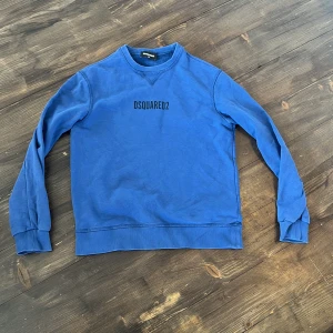 Blå sweatshirt från Dsquared2 - Säljer en blå sweatshirt från Dsquared2 med tryckt logga på bröstet. Tröjan har rund halsringning och långa ärmar. Ny pris 4000kr+. Hör av dig vid minsta fundering👍😁