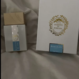 Bianco Latte Eau de Parfum från Giardini di Toscana - Exklusiv parfym i elegant vit flaska med träfärgat lock och gulddetaljer. Doften Bianco Latte kommer i en matchande vit kartong med guldkrans och blå etikett. Perfekt för dig som gillar lyxiga och unika dofter.