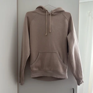 Beige hoodie med ficka - En enkel och stilren beige hoodie med huva och dragsko. Tröjan har en stor magficka och långa ärmar. Perfekt för en avslappnad look.