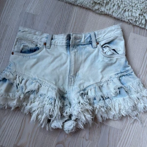 Ljusblå fransiga jeansshorts - Säljer ett par ljusblå jeansshorts från Monki med extremt fransiga kanter och klassisk femficksmodell. Shortsen har låg midja och är tillverkade i 100% bomull. Nästan aldrig använda köpte i somras