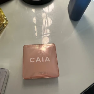 CAIA highlighter i champagnefärg - Säljer en CAIA highlighter i en lyxig, fyrkantig roséguldig dosa med spegel. Färgen är en skimrande champagne-ton som ger glow till ansiktet. Perfekt för att framhäva kindben och andra ansiktsdrag.