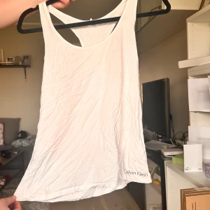 Vit linnetopp från Calvin Klein - Säljer en vit linnetopp från Calvin Klein med brottarrygg och logga nertill. Perfekt för varma dagar eller träning. Tunt och mjukt material som känns skönt mot huden.