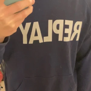 Blå hoodie från Replay - Säljer en blå hoodie från Replay med vit logga framtill. Tröjan har huva och en klassisk passform, perfekt för en avslappnad stil. Snygg och enkel att matcha med det mesta. Köpt på plick inte använd mycket