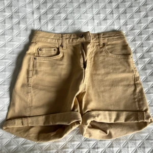 Beigea shorts från Pieces - Snygga beige shorts från Pieces med klassisk femficksdesign och uppvikta benslut. De har hög midja och stängs med dragkedja och knapp. Perfekta för varma dagar och enkla att matcha med olika toppar.