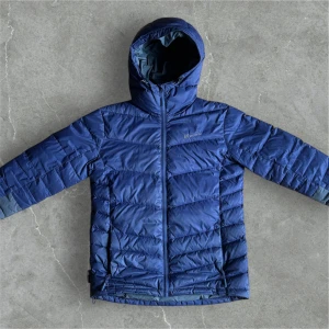 Blå dunjacka med huva från Skogstad - Säljer en blå dunjacka från Skogstad med huva och dragkedja framtill. Jackan är quiltad och har lång ärm. Perfekt för kyliga dagar och enkel att matcha med olika outfits.