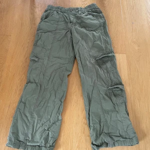 Gröna cargobyxor med fickor - Säljer ett par gröna cargobyxor med flera stora fickor på sidorna och resår vid bensluten. Perfekta för en avslappnad och praktisk stil. Byxorna har normal passform och stängs med knapp och dragkedja.