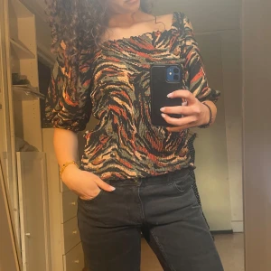 Mönstrad blus med puffärm - Säljer en snygg blus med tigerinspirerat mönster i svart, olivgrön, brun och beige. Blusen har puffiga trekvartsärmar och en smickrande fyrkantig ringning. Sitter lite lösare på mig runt midjan och ärmarna faller ibland ner på axlarna, men går finemang att sy så att de sitter tightare😊