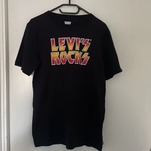 Svart t-shirt med tryck från Levi's - Svart t-shirt från Levi's med  'LEVI'S ROCKS'-tryck på bröstet. Klassisk passform med rund hals och korta ärmar. Helt oanvänd och har storleken S. Priset kan diskuteras.