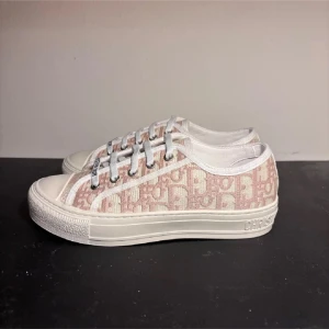 Christian Dior sneakers med monogram - Säljer ett par snygga sneakers från Christian Dior med rosa och vita monogramdetaljer. Skorna har vita snören med märkets logga och en tjock vit sula med stjärndetalj undertill. Perfekta för dig som gillar exklusiva och trendiga skor.