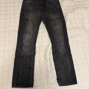 Svarta jeansbyxor Levis 501 W30 L32 - Klassiska svarta Levis 501 jeans med raka ben och femficksdesign. Byxorna har knappgylf och tydlig Levis-lapp bak i midjan. Passar dig som gillar en tidlös och avslappnad stil.