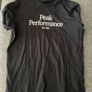 Svart t-shirt från Peak Performance - Svart t-shirt från Peak Performance med vit logga och text 'Est. 1986' på bröstet. Klassisk rund hals och korta ärmar. Perfekt för en avslappnad stil.