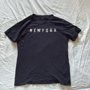 Blå t-shirt  - Svart t-shirt  med vitt tryck 'NEW YORK' över bröstet. Klassisk rund hals och korta ärmar. Skriv för frågor 
