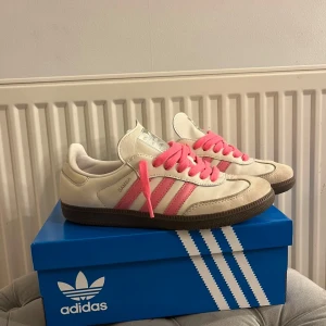 Adidas Samba Rosa - Säljer ett par Adidas Samba sneakers i vitt med rosa ränder och rosa skosnören. Skorna har klassisk brun sula och är tillverkade i skinn och syntet. Perfekta nu flr våran och en mycket skön sko i garanterad kvalité!