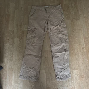 Beiga cargopants från Perfect Jeans - Snygga beiga cargopants från Perfect Jeans med flera praktiska fickor på sidorna och bak. Byxorna har rak passform, bälteshällor och dragkedja framtill. Perfekta för en avslappnad och trendig look.