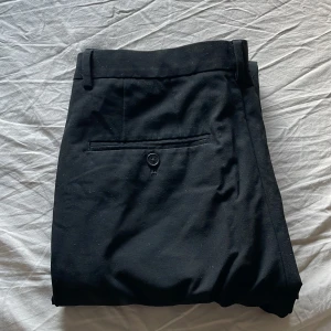 Svarta kostymbyxor från H&M slim fit - Svarta kostymbyxor från H&M i slim fit-modell. Byxorna har klassiska fickor, bälteshällor och en knapp bak. Snygg rak passform som funkar till skjorta eller t-shirt.